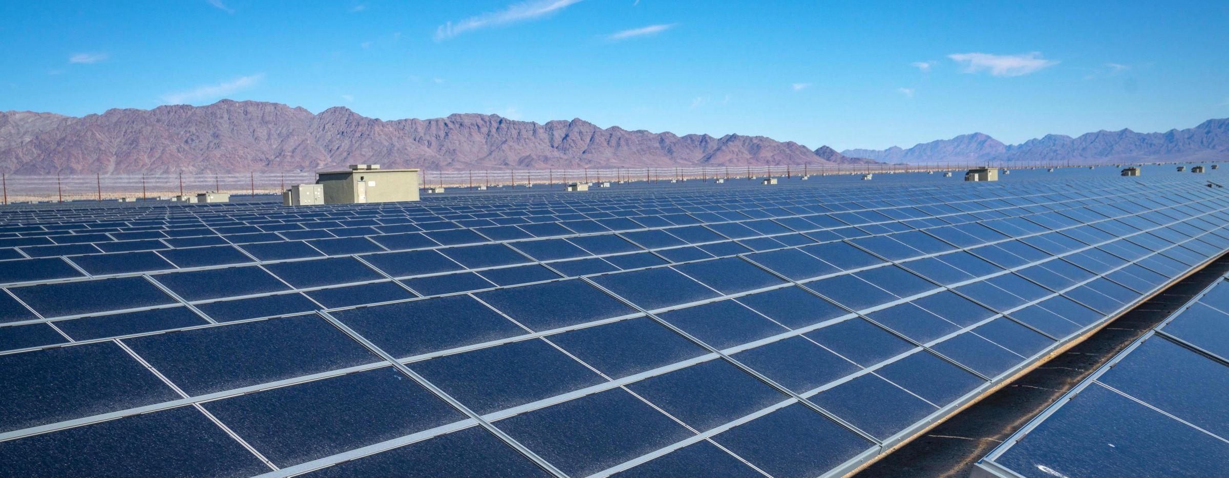 Rows of solar panels in the California desert, with mountains behind